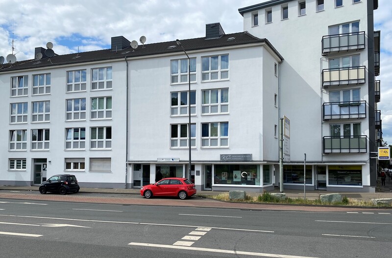 Straßenansicht der modernisierten Gebäude, unten ein Ladenlokal, davor geparkte Autos.