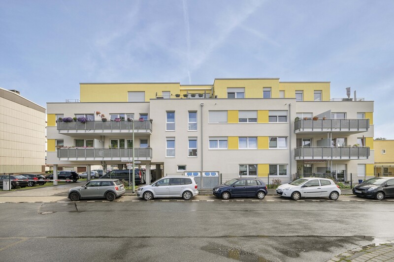Straßenansicht des Neubaus, Fassade gelb und weiß, 3 Stockwerke, vor dem Haus Autos. 