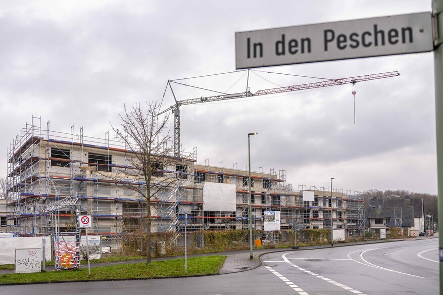 Ein Riegel von eingerüsteten Mehrfamilienhäusern auf einer Baustelle. Im Vordergrund das Straßenschild "In den Peschen".