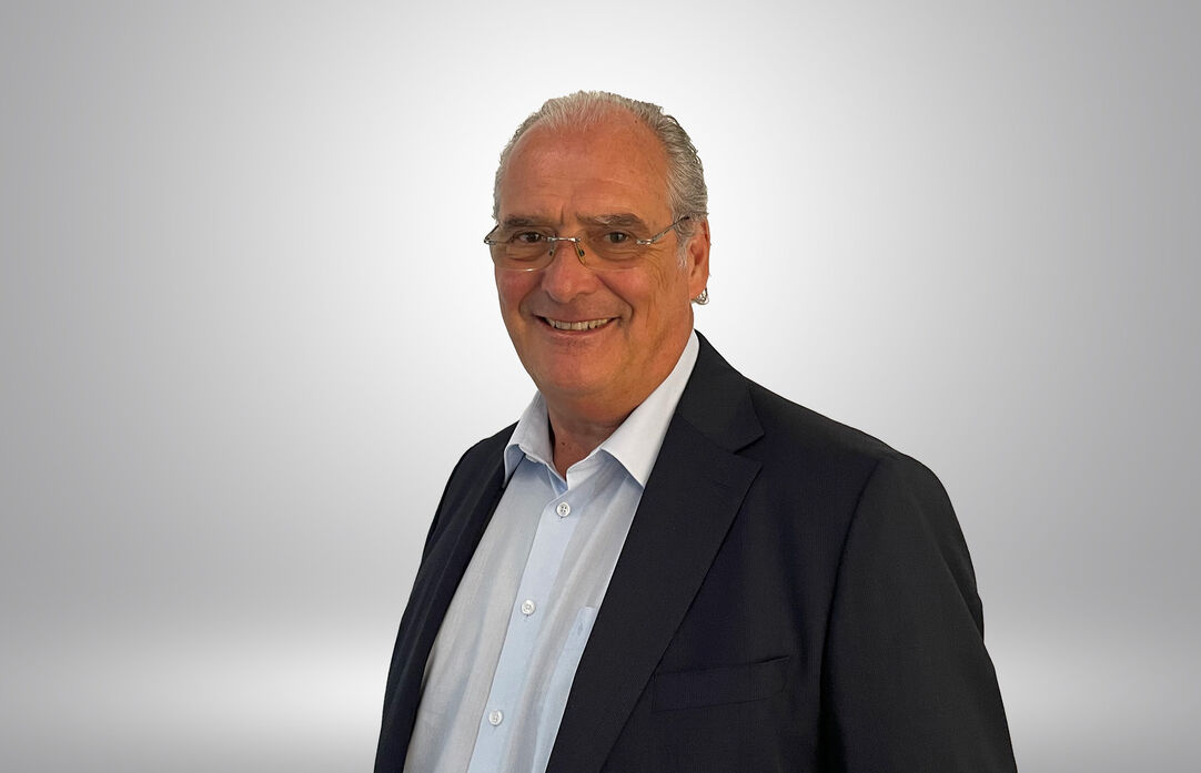 Ein lächelnder Mann mit Brille und Anzug schaut in die Kamera. 