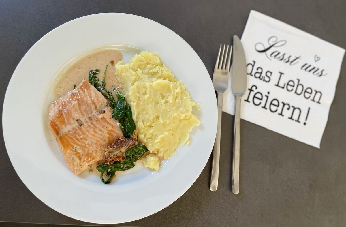 Auf einem Teller ein Lachsfilet mit Sauce und Kartoffelstampf, dazwischen etwas Blattspinat