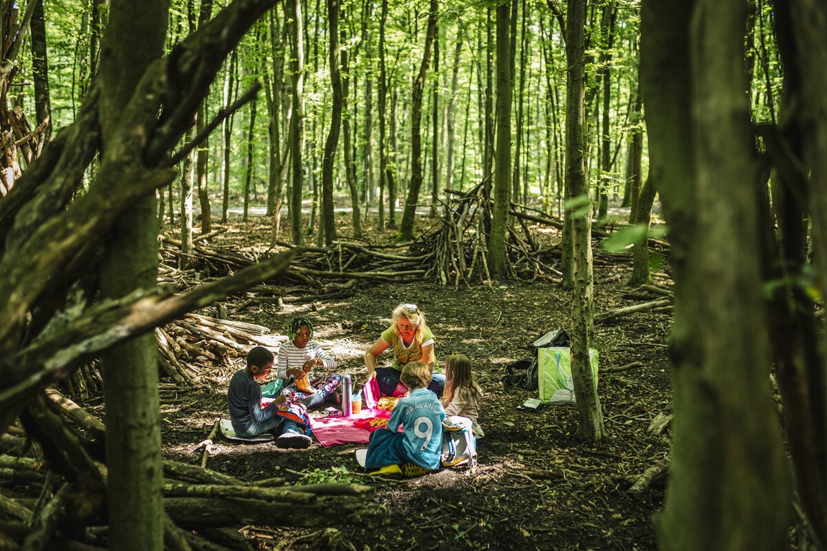 Szene im grün-dunklen Wald, eine Frau sitzt mit Kindern im Kreis