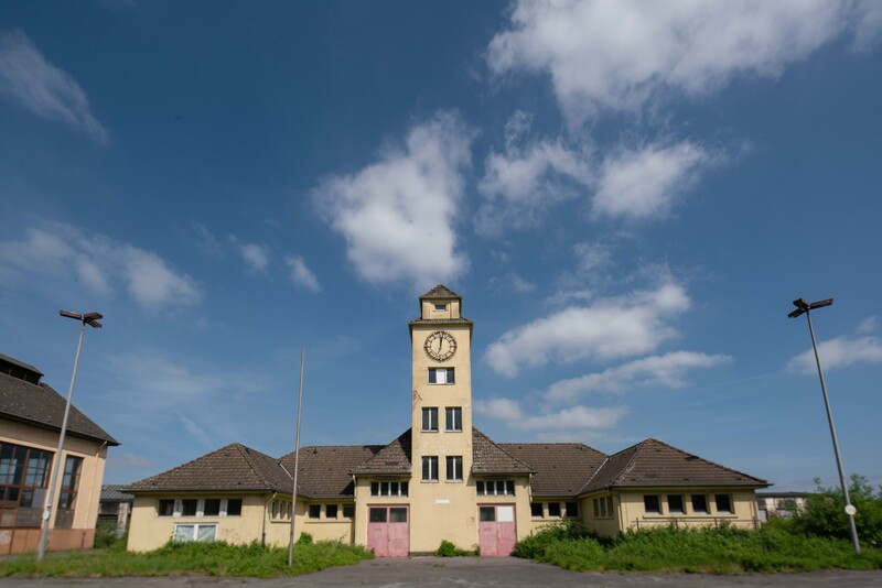 Ansicht der denkmalgeschützten Feuerwache mit dem markanten Uhrenturm in der Mitte. Blauer Himmel mit Wolken