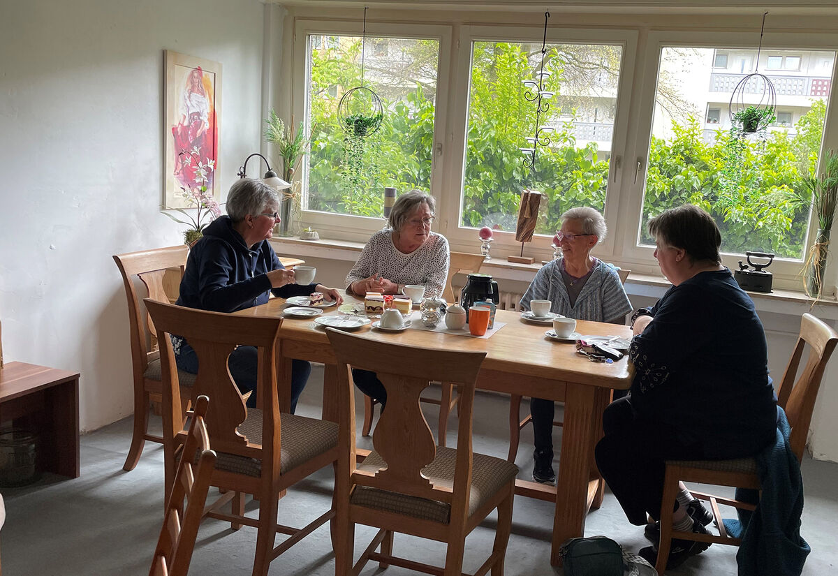 Vier ältere Damen sitzen an einem Holztisch in einem hellen Raum und unterhalten sich angeregt bei Kaffee und Kuchen.