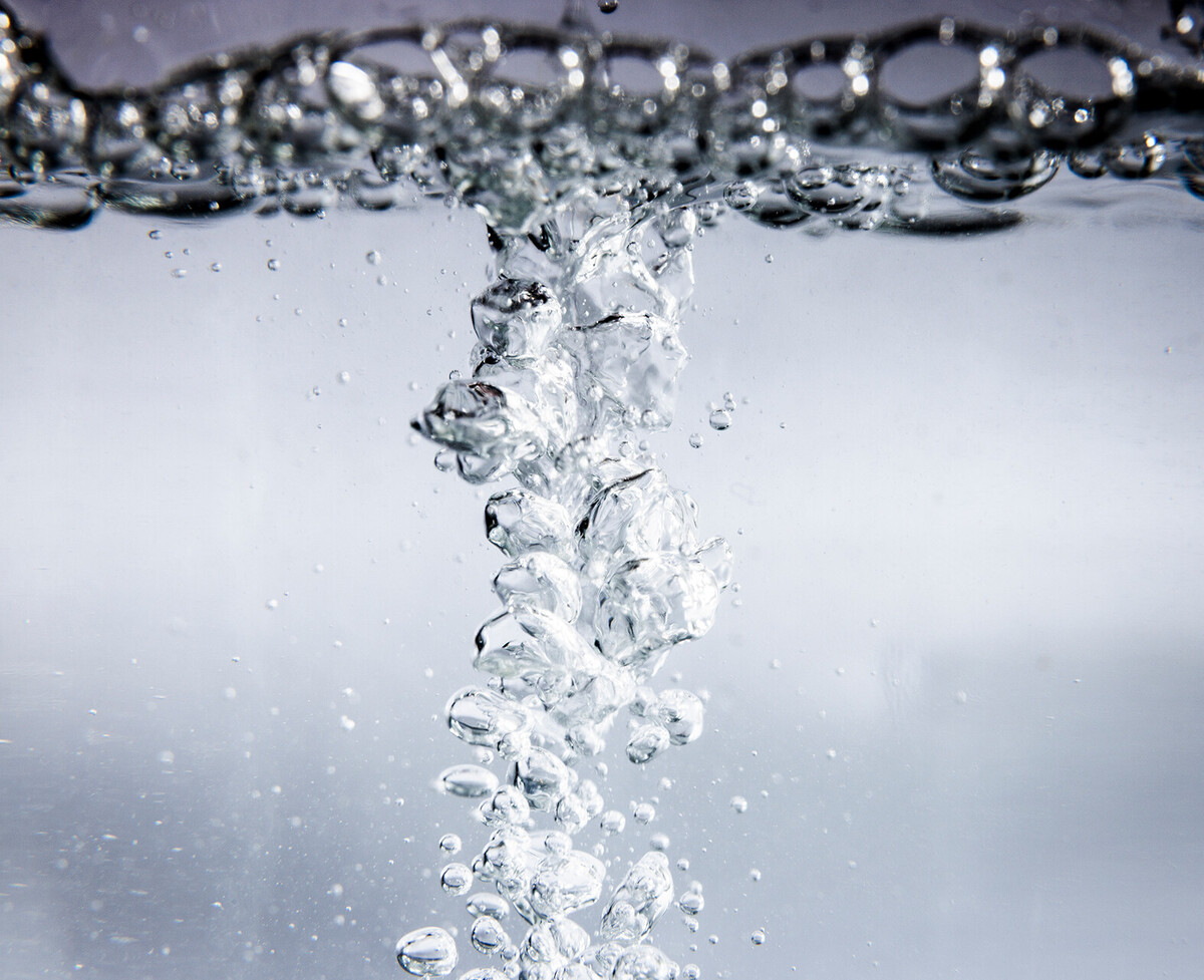 Blasen steigen in klarem Wasser auf, die Wasseroberfläche ist ebenfalls voller Blasen.