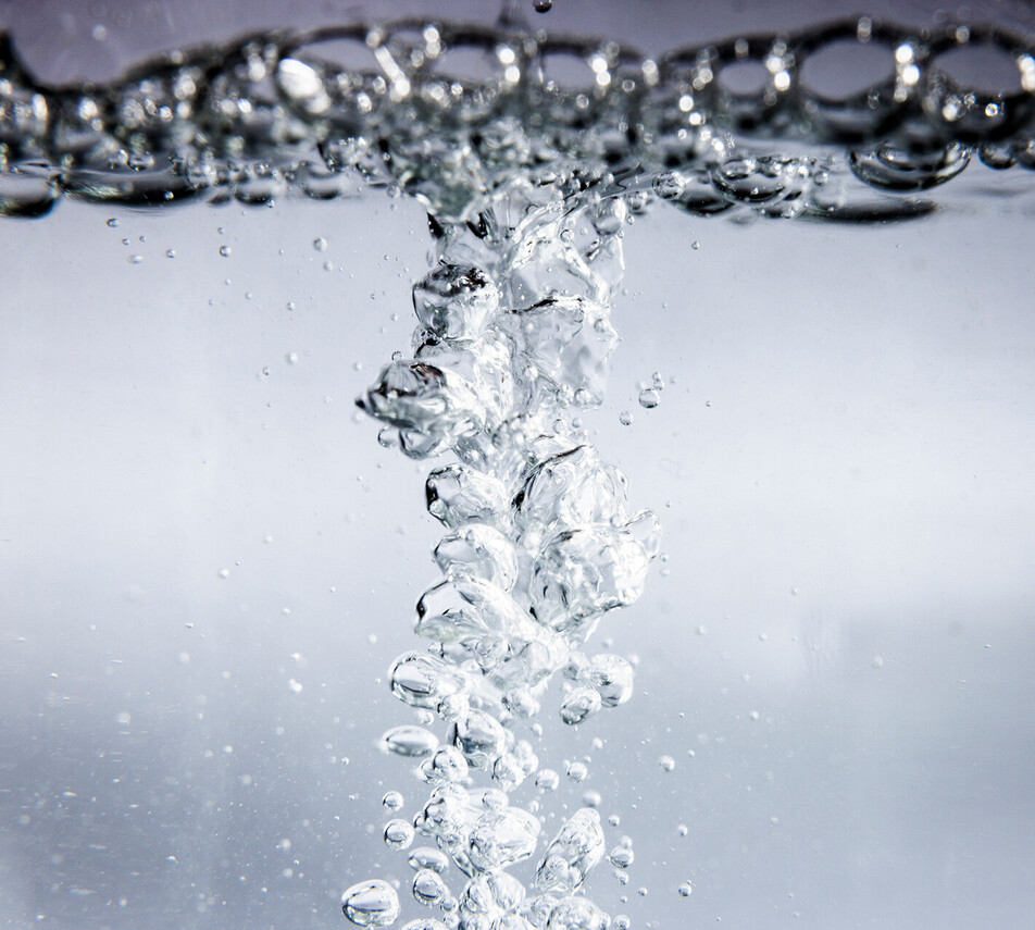 Blasen steigen in klarem Wasser auf, die Wasseroberfläche ist ebenfalls voller Blasen.