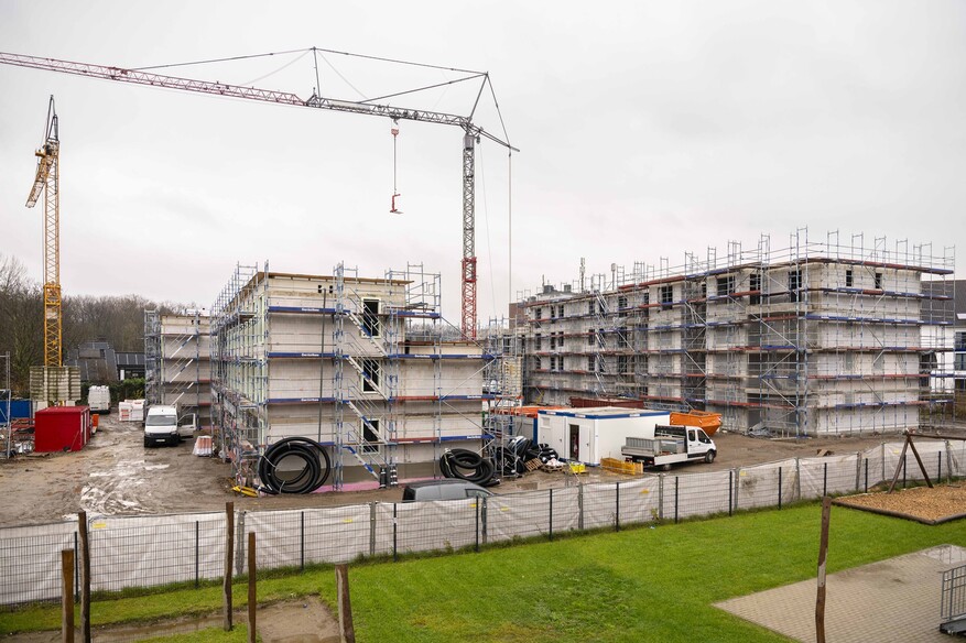 Zwei eingerüstete Mehrfamilienhäuser auf einer Baustelle. Zwei Kräne stehen in der Nähe. Im Vordergrund ein Stück Wiese.