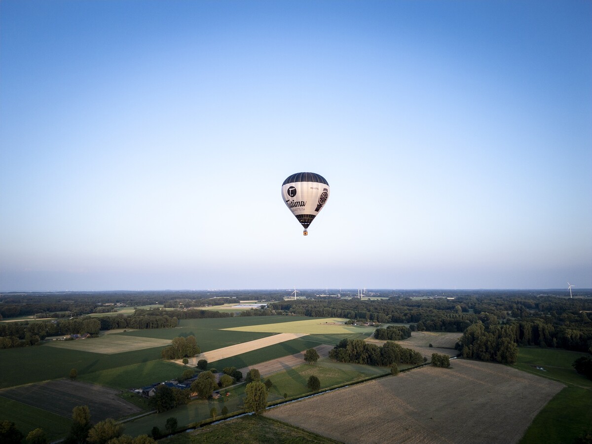 Ein Heißluftballon schwebt über eine leicht hügelige Landschaft. Himmel in leichter Dämmerung.