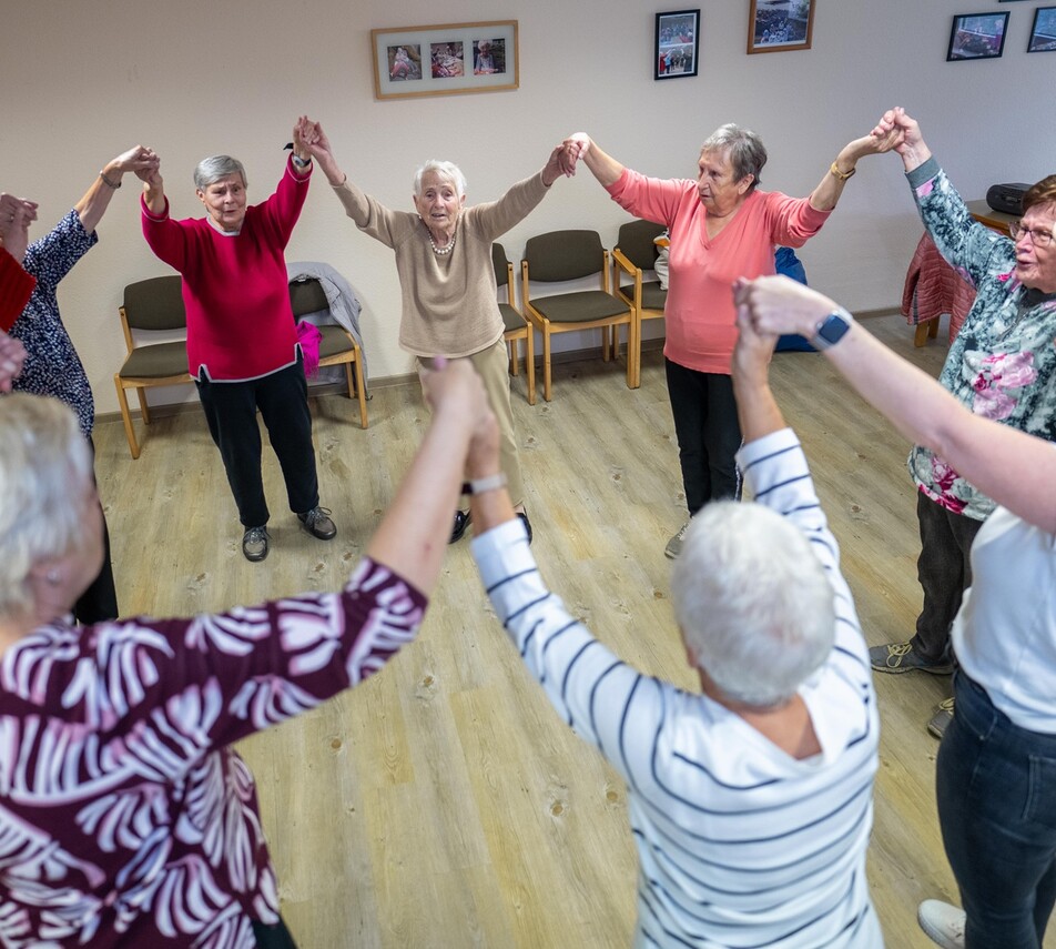 Eine Gruppe älterer Damen hält sich an den Händen und bildet dabei einen Kreis.