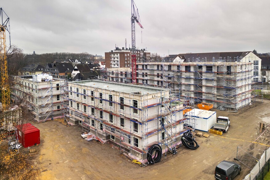 Blick von schräg oben auf mehrere eingerüstete Mehrfamilienhäuser auf einer Baustelle, in der Mitte zwischen den Häusern ein Kran.